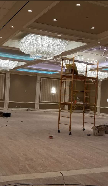 Commercial banquet hall stripped of flooring with scaffolding set up under chandeliers