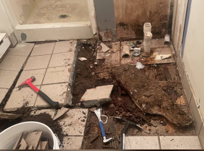 Damaged bathroom tile and subfloor removed around plumbing rough-in