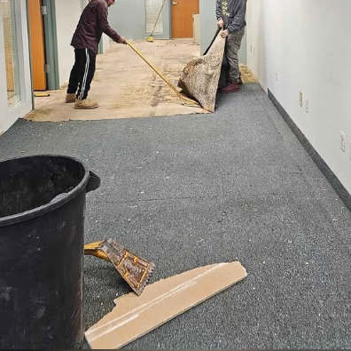 Two workers pulling up commercial carpet in an office corridor
