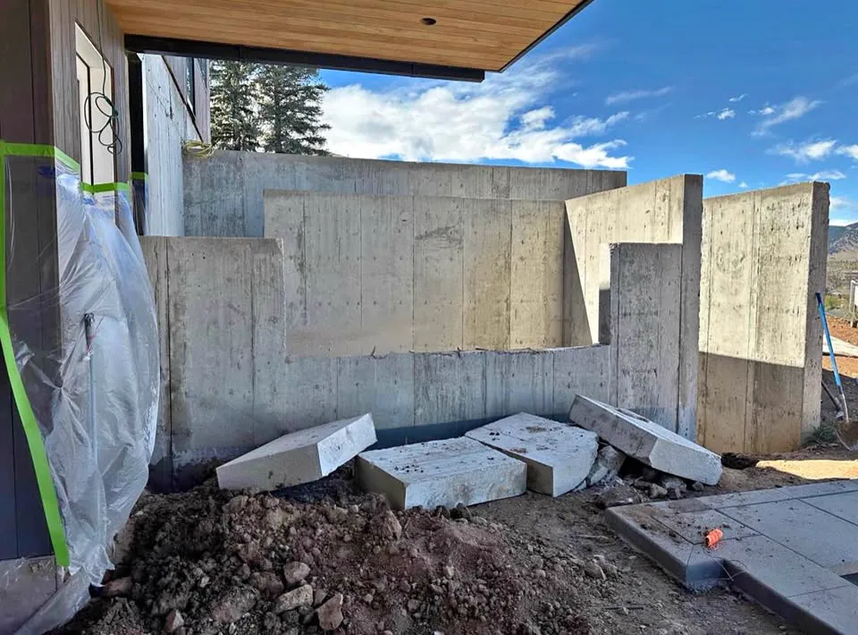 Poured concrete foundation wall with saw-cut sections removed and cut blocks lying beside a patio
